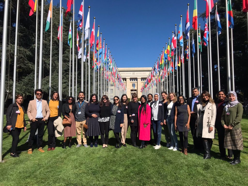 Students standing in front of two rows of flags in front of the Palais des Nations in Geneva